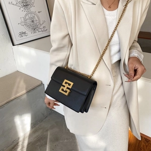 Détail d'un sac bandoulière noir avec chaîne dorée et fermoir carré sur modèle