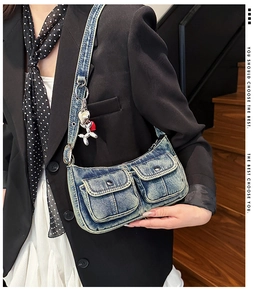 Detail of blue denim shoulder bag with utility pockets and silver balloon dog pendant