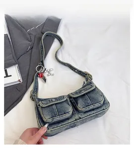 Detail view of denim shoulder bag featuring buckle pockets and a silver dog charm accessory