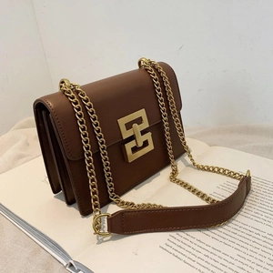 Sac bandoulière rétro en cuir marron foncé avec boucle dorée et chaîne sur des livres
