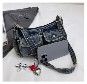 Detail of vintage denim baguette bag with silver grommets and heart charms beside a phone