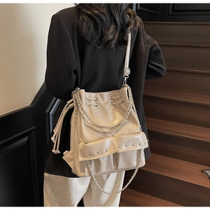 Chic beige bucket bag with silver chains and rivets on vintage wooden stairs