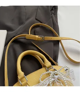 Detail of yellow pebbled leather handbag featuring pearl and lace bow decoration