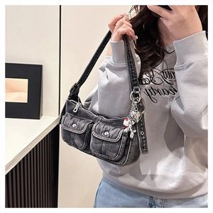 Detail of dark gray denim shoulder bag with utility pockets and a metal bear charm