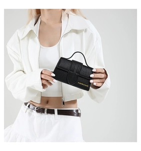 Detail of black mini handbag in pebble grain leather held by model in white outfit