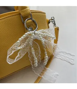 Detail of white pearl lace bow charm with silver clasp on yellow leather handbag