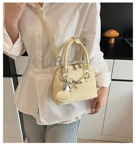 Gros plan du sac bandoulière beige avec charm cœur et détails de chaîne en métal argenté