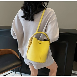 Gros plan d'un sac seau en cuir jaune avec motif litchi et détail foulard en soie
