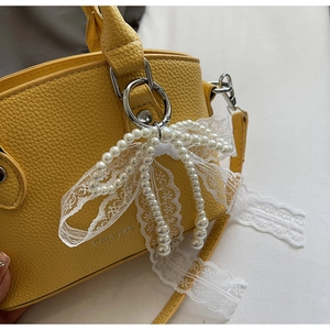 Detail of yellow lychee leather bucket bag with pearl lace bow charm and silver logo