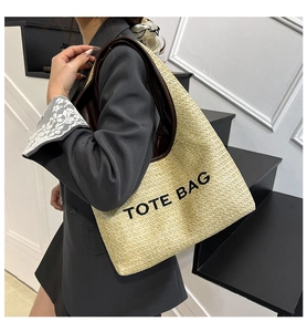Detail of raffia tote bag with brown leather straps and black printed lettering text