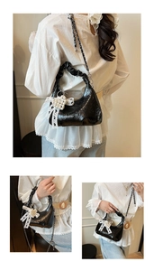 Detail of black glossy pleated cloud bag featuring pearl bow charm and silver chain strap