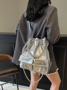 Silver metallic bucket bag with studs and chain straps shown on model in grey suit
