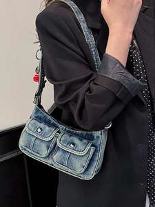 Vintage blue denim shoulder bag with flap pockets and red charm accessory on model