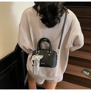 Detail of black lychee grain leather bucket bag with pearl lace bow charm accent