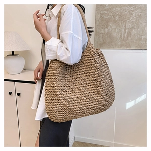 Close-up of a beige woven straw tote bag worn by a model in a minimalist setting