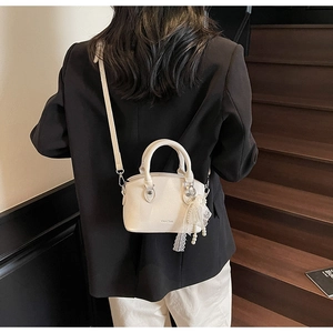 White lychee leather bucket bag with lace pearl charm shown on a dark staircase background