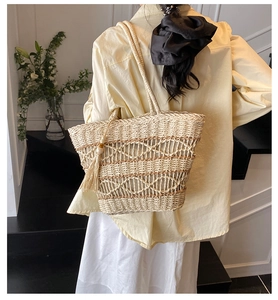 Detail of bohemian straw woven tote bag featuring hollow diamond patterns and tassel charm