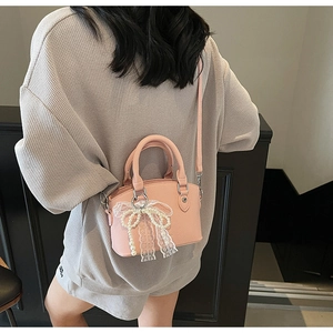 Detail of pink lychee leather bucket bag with lace bow and pearl charm on shoulder
