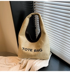 Close-up of woven straw tote bag featuring contrast piping and TOTE BAG text print
