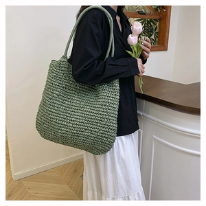 Detailed close-up of large green woven straw tote bag with integrated shoulder straps