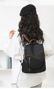 Rear view of woman wearing a black minimalist backpack with brown leather straps and zip pocket