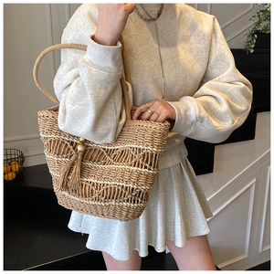 Close-up of bohemian hollow woven straw tote bag featuring decorative tassel with wood beads