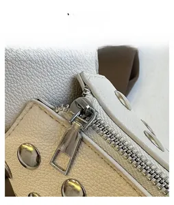 Detail view of smooth silver metal zipper and rivets on white lychee grain leather bag