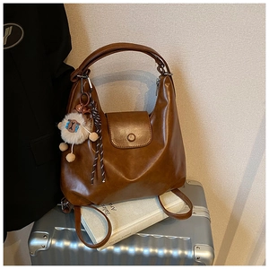 Détail d'un sac à dos en cuir marron avec breloque mouton posé sur une valise argentée
