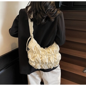 Close-up of cream pleated cloud bag on shoulder showing soft texture and modern style