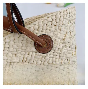 Detail of uniform white stitching on brown faux leather handles of a woven straw bag
