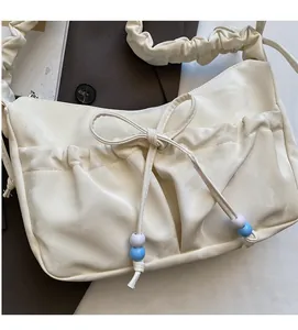 Dettaglio della borsa a spalla plissettata bianco crema con fiocco e ciondoli