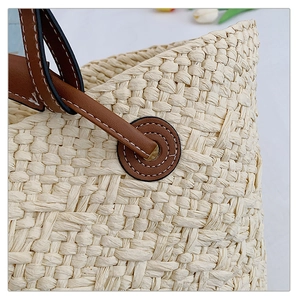 Detail of woven straw bag showing cream fiber texture and brown leather handle