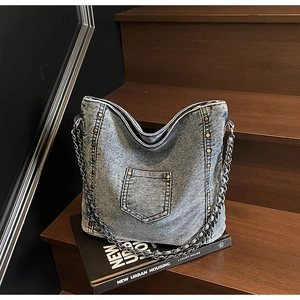 Detail of vintage denim crossbody bag with metal rivets on dark wooden steps