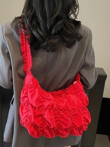 Red ruched cloud shoulder bag featuring pleated texture and integrated wide strap on model