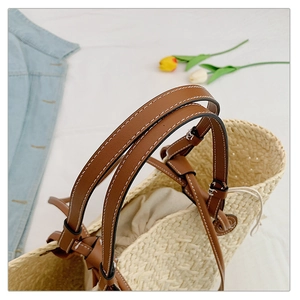Detail of beige woven straw tote bag featuring leather handles and drawstring inner lining