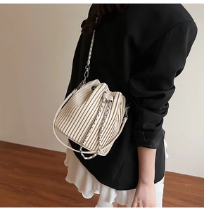 Detailed side view of an elegant cream pleated bucket bag with chain strap worn by a model
