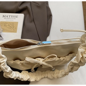 Dettaglio della borsa a nuvola color crema con fiocco su uno sfondo di libro d'arte