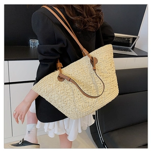 Detail of hand-woven straw tote bag with brown leather shoulder straps on a female model