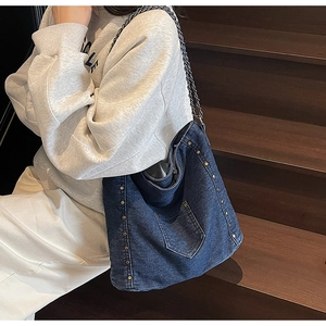 Detail of vintage denim hobo bag with bronze rivets and metal chain strap on model