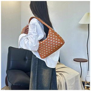 Brown leather underarm bag featuring silver rivets worn by a model in a cozy room
