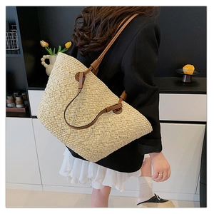 Detailed view of woven straw tote bag texture with brown leather handle and large capacity