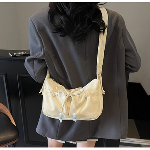 Dettaglio borsa a nuvola beige con fiocco e perle blu-bianche indossata da modella