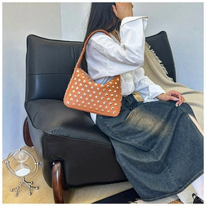 Detail view of orange studded underarm bag worn by a model in a casual setting