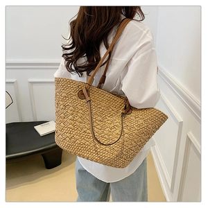 Detail of woven straw tote bag with brown leather handles on a female model