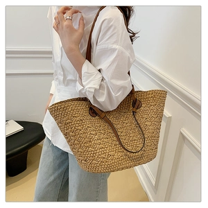 Detail of woven straw tote bag with brown leather straps shown on a model