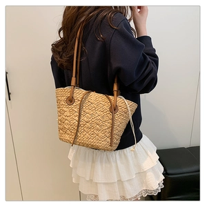 Detail of woven straw tote bag featuring leather shoulder straps and drawstring closure