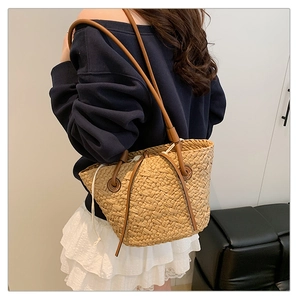 Detail of woven straw tote bag featuring brown leather shoulder straps and canvas inner lining