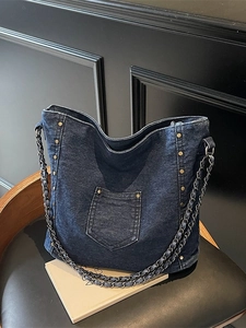Vintage navy denim tote bag with metal studs and chain strap on a black leather seat