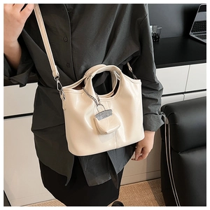 Close-up of off-white glossy handbag with mini charm and silver chain strap details