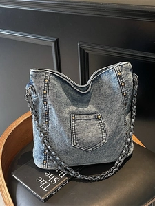 Vintage denim crossbody bag with bronze studs and metal chain strap on a black chair